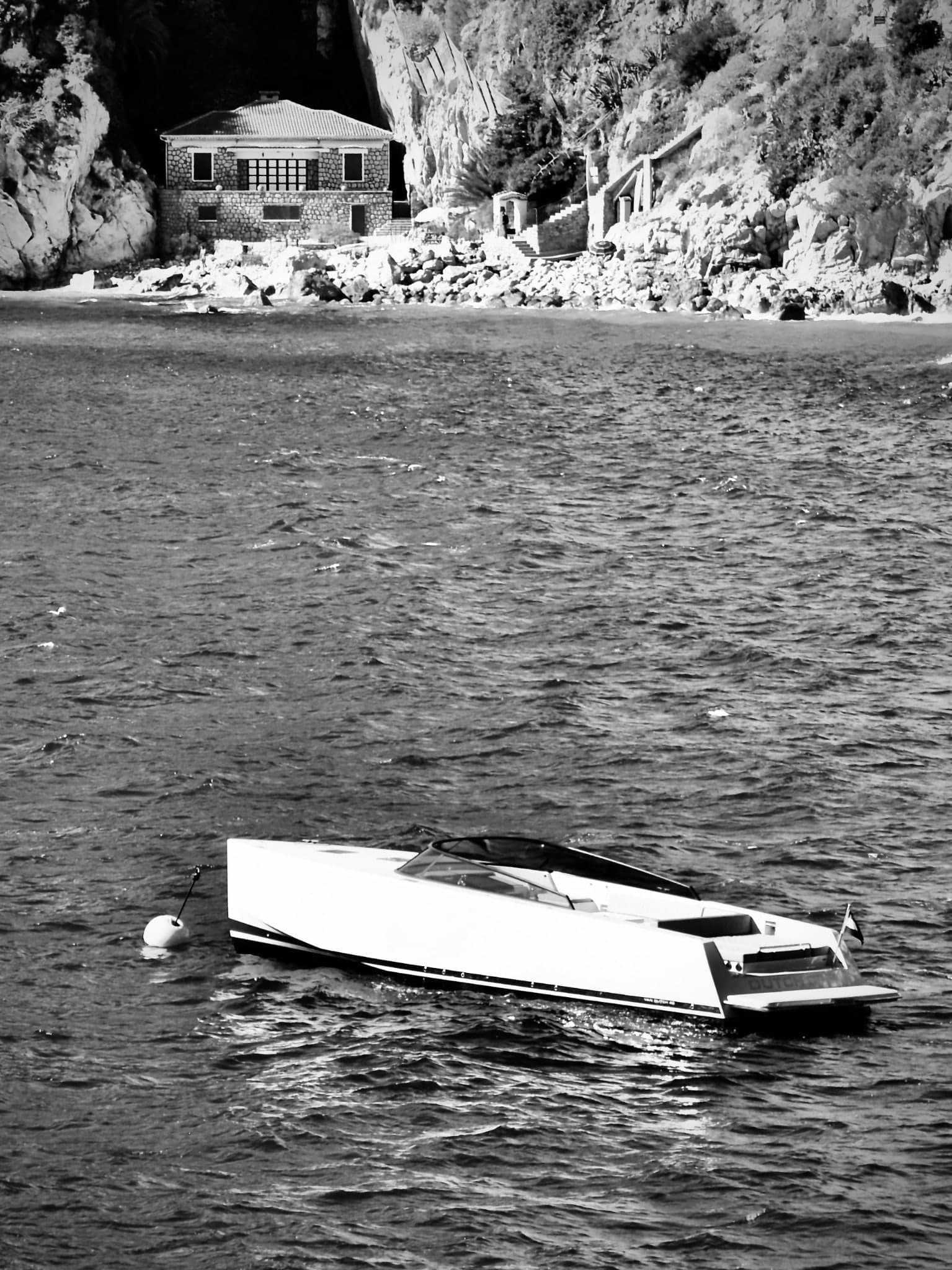 Motorboot vor steiler Felsküste und einzelnen Häusern in Schwarz-Weiß