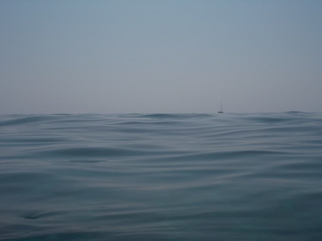 Entferntes Segelboot hinter sanften blauen Meereswellen